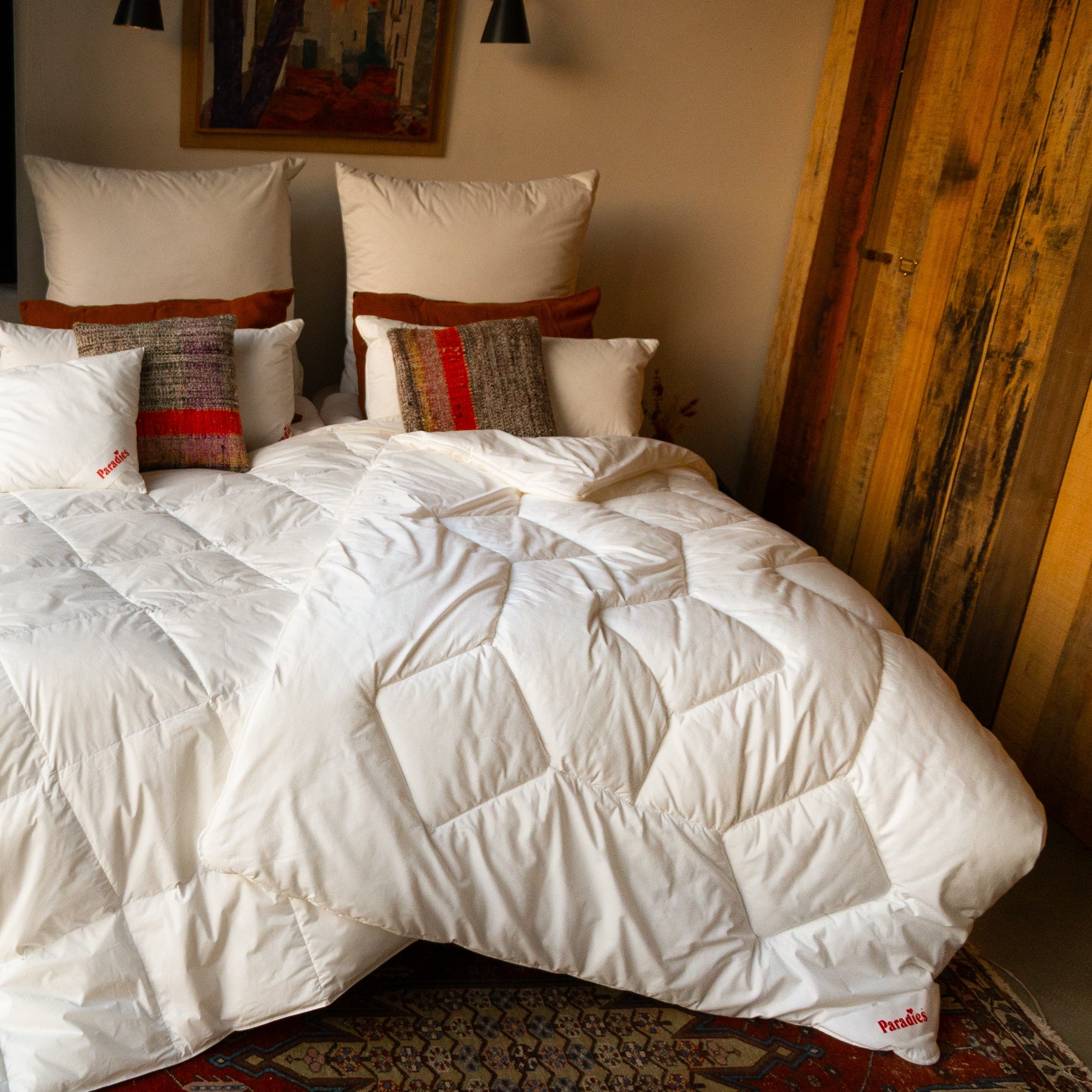 Doppelbett mit weißer Steppdecke und mehreren Kissen vor einer Holzpaneelwand