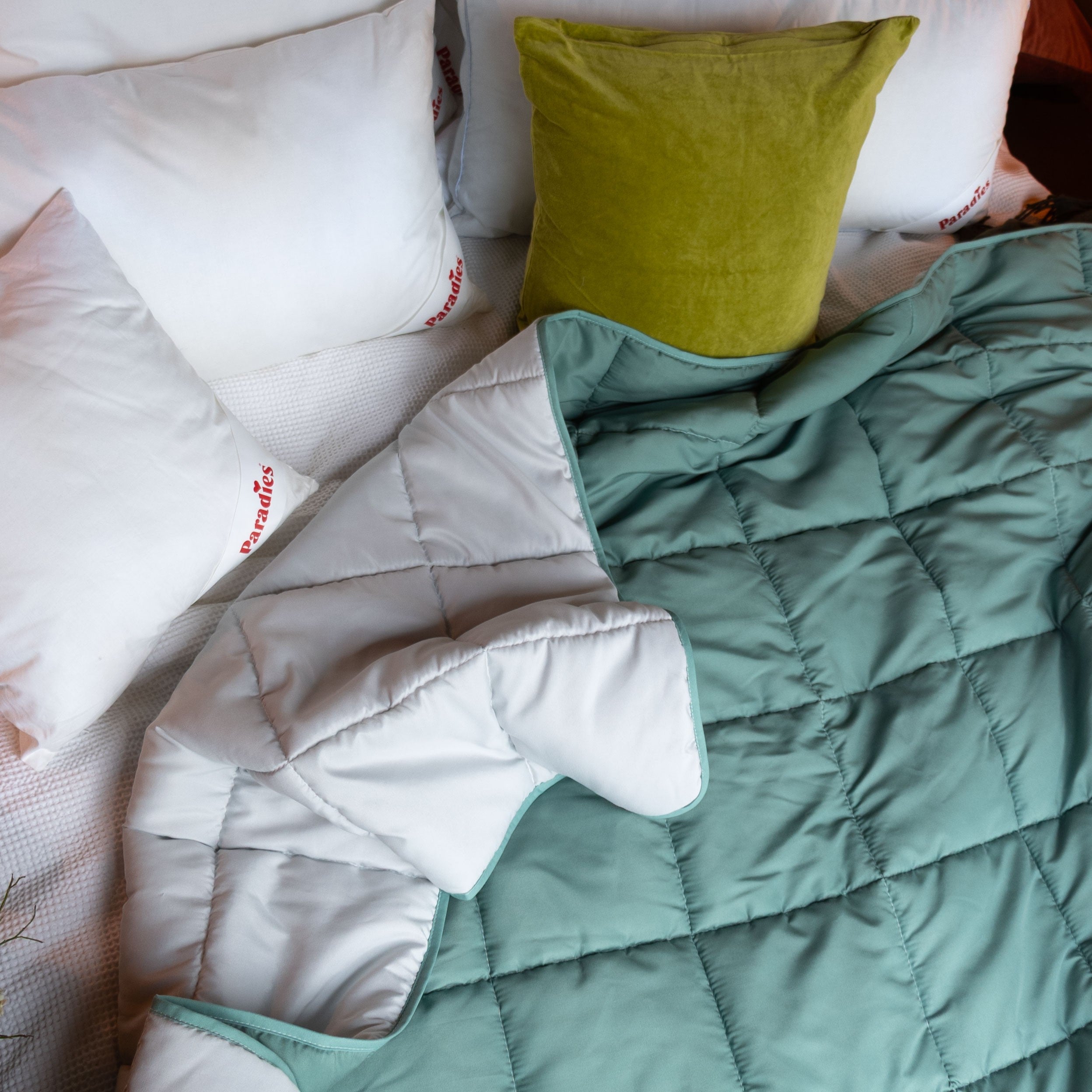 Bett mit weißen Kissen und grünem Kissen sowie einer zweifarbigen Steppdecke in Grün & Grau